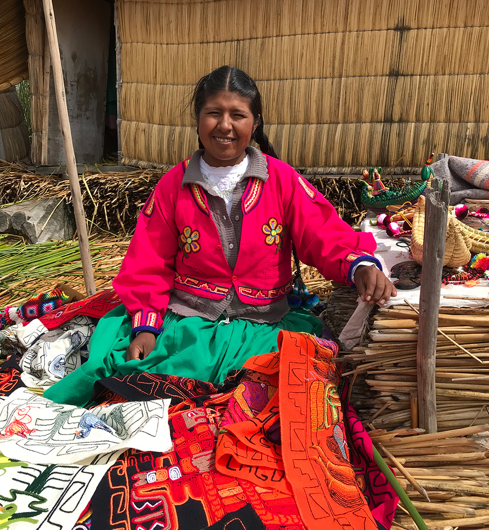 Peruansk kvinna i färgglada kläder, framför hus av vass